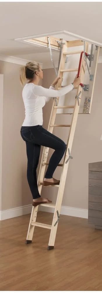 A woman climbing a wooden folding loft ladder up through an open loft hatch